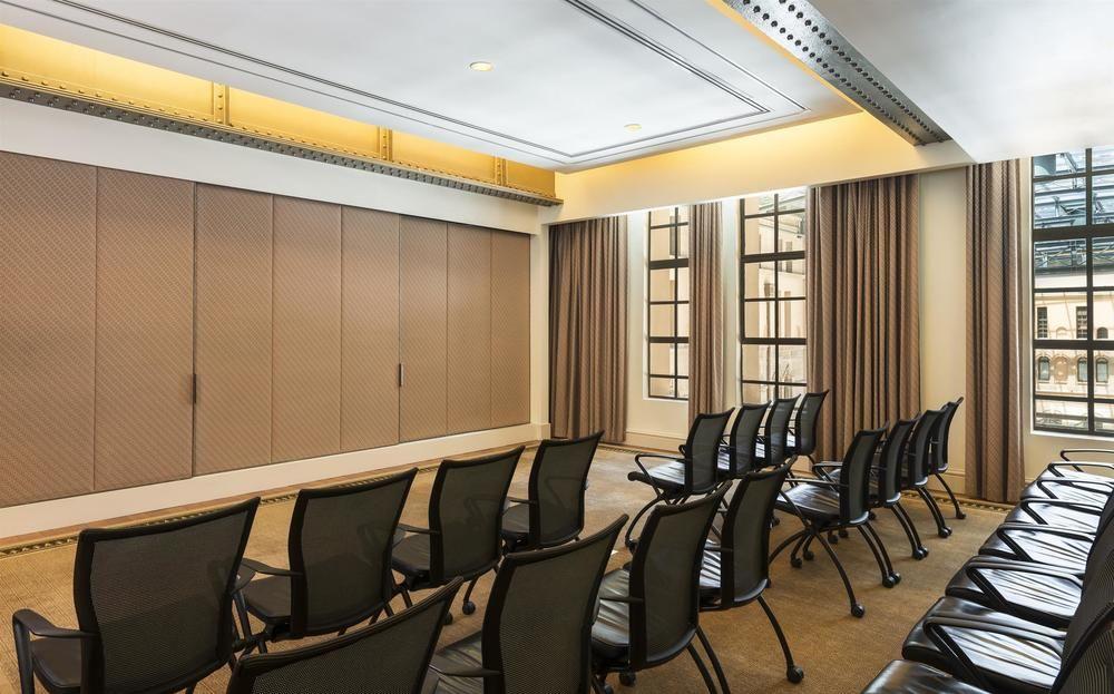 더 풀러턴 호텔 시드니 외부 사진 The photo shows a modern conference room or meeting space. There are several rows of black chairs arranged facing a wall. The walls appear to have a beige tone with large windows adorned with curtains, allowing natural light to enter. The ceiling is 