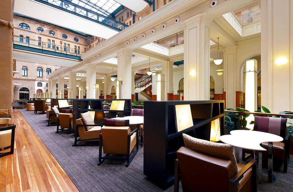 더 풀러턴 호텔 시드니 외부 사진 The photo features a spacious and well-lit interior of a lounge or café area, characterized by high ceilings and large windows that allow natural light to flood the space. The design includes elegant architectural details, such as tall columns and an