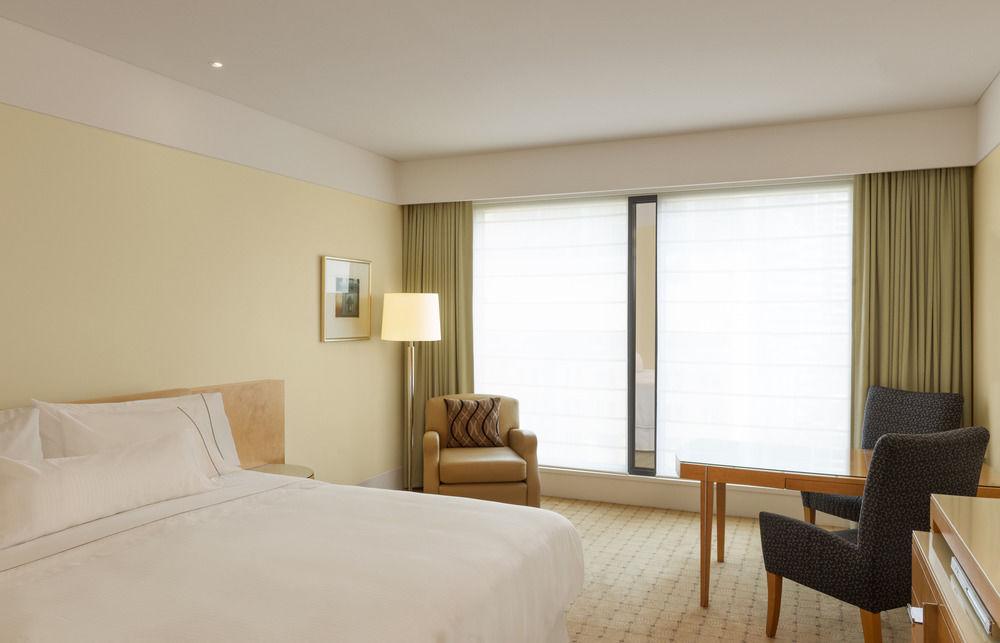 더 풀러턴 호텔 시드니 외부 사진 The photo shows a modern hotel room. The decor features soft, neutral colors, creating a calm and inviting atmosphere. There is a large bed with crisp white linens against one wall. A bedside lamp stands on a small table next to the bed. 

Near the w