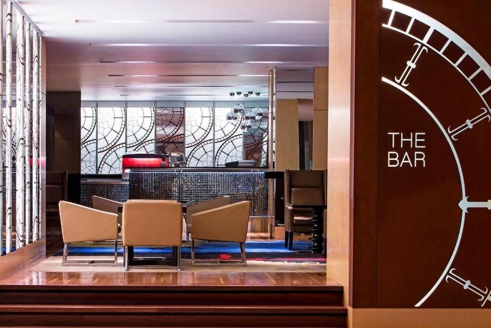 더 풀러턴 호텔 시드니 외부 사진 The photo shows a modern bar area with a stylish and elegant design. In the foreground, there are several upholstered chairs arranged around a small table. The bar counter is visible in the background, featuring a sleek design and various lighting el