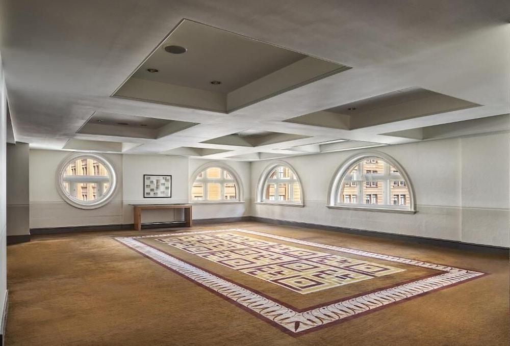 더 풀러턴 호텔 시드니 외부 사진 The photo shows a spacious, well-lit room with a contemporary design. The ceiling is divided into sections with recessed lighting. There are several rounded windows that allow natural light to enter, creating an airy atmosphere. A large area rug with